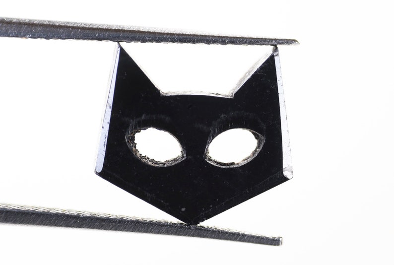 May include: Black cat-shaped charm with cut-out eyes, held by tweezers.