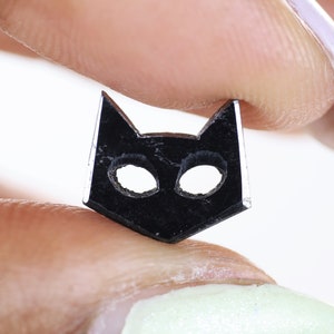 May include: A black cat-shaped charm with cut-out eyes, held between two fingers.