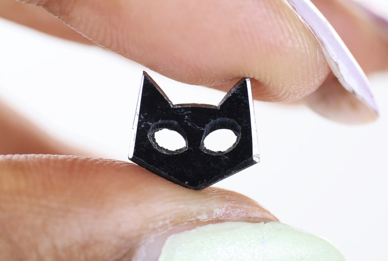 May include: A black cat-shaped charm with cut-out eyes, held between two fingers.
