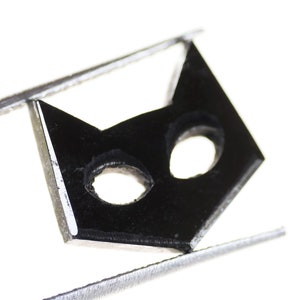 May include: A black cat face cutout with two holes for eyes, held in a pair of silver tweezers.
