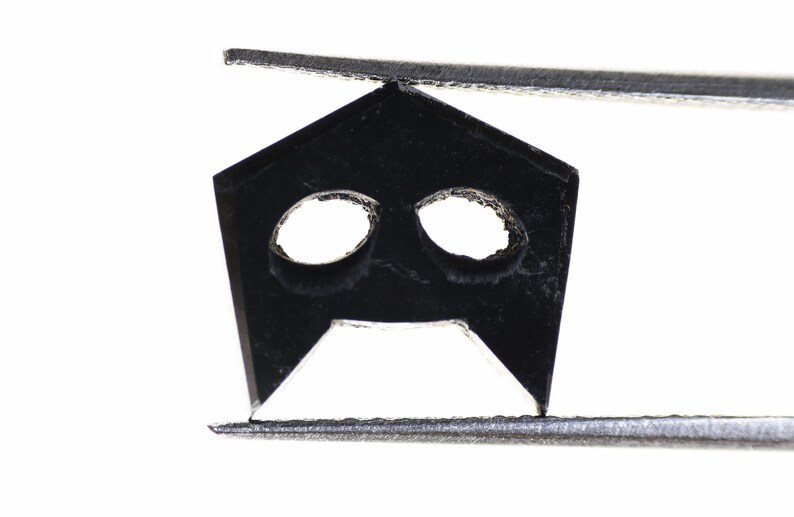 May include: A black metal object with two holes and a pointed tip, held by silver tweezers.