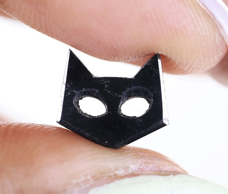 May include: A black cat-shaped charm with cut-out eyes, held between two fingers.