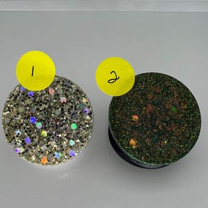 Peut inclure: Deux poignées de téléphone rondes avec une finition pailletée. La première poignée est dorée avec des paillettes irisées et la deuxième poignée est verte avec des paillettes irisées.