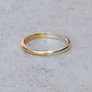 May include: A simple gold and silver wedding band. The band is split in half, with one side gold and the other side silver.