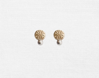 Può includere: Un paio di orecchini in oro e argento con un design circolare testurizzato. Gli orecchini hanno una piccola perla d'argento appesa alla parte inferiore.
