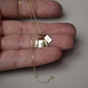 Pu&ograve; includere: Una collana a catena in oro con quattro piccoli ciondoli rettangolari in oro. Tre dei ciondoli sono stampati con le lettere M, A e C, mentre il quarto ciondolo &egrave; stampato con la lettera A. I ciondoli pendono da una sottile catena a maglie d'oro.