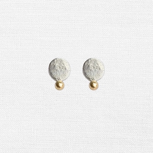 May include: A pair of silver earrings with a textured round disc and a small gold bead hanging from each disc.