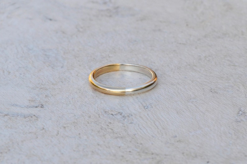 May include: A simple gold and silver wedding band. The band is split in half, with one side gold and the other side silver.
