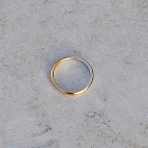 May include: A simple gold band ring on a white textured surface.