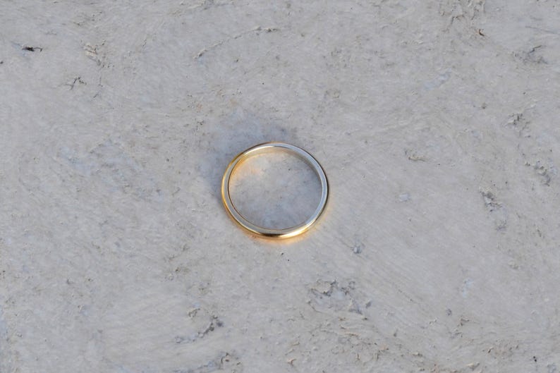 May include: A simple gold band ring on a white textured surface.