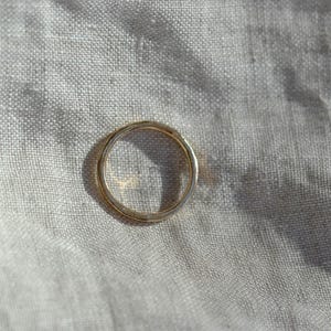 Puede incluir: Un anillo de banda de oro circular simple con un acabado liso y pulido. El anillo presenta un perfil redondeado y consistente en toda su circunferencia, mostrando un tono amarillo met&aacute;lico c&aacute;lido que refleja la luz en su superficie.