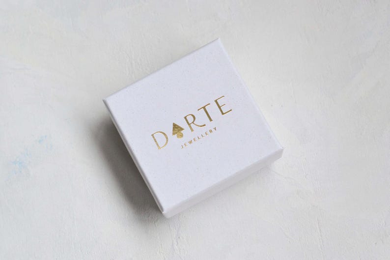 Pu&ograve; includere: Una scatola portagioie quadrata in cartone bianco con il testo in lamina d'oro DARTE JEWELLERY stampato sul coperchio. La lettera A nella parola DARTE &egrave; sostituita da una piccola icona a forma di albero triangolare dorato. Finitura opaca.