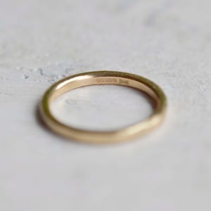 Puede incluir: Un anillo de banda de oro liso con un perfil redondeado. La superficie interior del anillo presenta una serie de peque&ntilde;os sellos grabados que son visibles tras una inspecci&oacute;n detallada, indicando la pureza del metal y su origen.