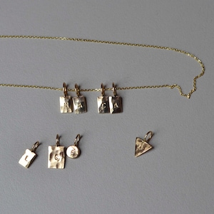 Pu&ograve; includere: Una collana a catena dorata con quattro ciondoli rettangolari stampati con le lettere N, A, C e A. Sotto la collana ci sono quattro ciondoli sciolti: un piccolo rettangolo con L, un rettangolo grande con C, un cerchio piccolo con E e un triangolo con M.