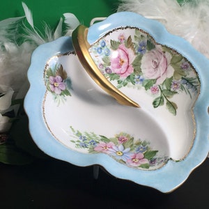 May include: A divided, leaf-shaped dish with a pale blue rim and a gold handle. The dish is decorated with pink and purple floral designs. The rim has a gold trim. The dish is likely made of porcelain.