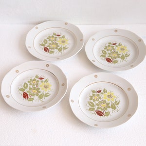 May include: Four white ceramic plates with a floral design. Each plate features a central bouquet of yellow and green flowers with red accents. A gold rim and small gold starbursts complete the design.