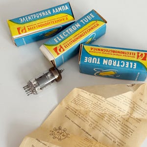 May include: An assortment of vintage electron tubes and packaging. The boxes are blue and yellow with Cyrillic text and the words "ELECTRON TUBE". A sheet of paper with technical diagrams and text is also present.