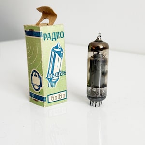 Op de afbeelding: Vintage vacuümbuis en de originele doos. De doos is lichtgroen met het woord "Радио" en een schema. De buis is van helder glas met zichtbare interne componenten.