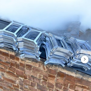 May include: A stack of silver metal frames, likely for concrete construction, sits on a brick wall. The frames are stacked in a staggered pattern, creating a visually interesting composition.