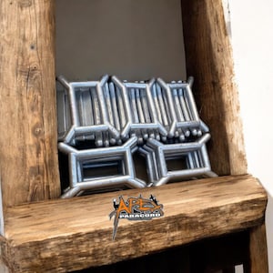 May include: A close-up of a stack of silver metal D-rings. The rings are arranged in a neat pile and are all the same size. The rings are in a wooden shelf with the text "APEX PARACORD" visible below.