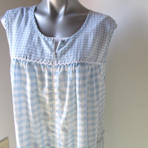 May include: A light blue and white checkered sleeveless robe with a full-length zipper. The robe features a rounded neckline and a white lace trim detail. The top portion of the robe has a houndstooth pattern.