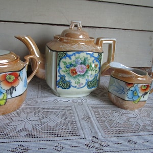 Burnt orange tea pot, creamer and sugar container. Handpainted floral pattern made in Japan, midcentury post WWII.
