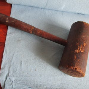 May include: A wooden mallet with a brown handle and a dark brown head. The head has a slightly rounded shape and is slightly worn.