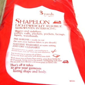 May include: A white package with red text that reads "3 yards 18" wide" and "SHAPELON LIGHTWEIGHT FUSIBLE NON-WOVEN INTERFACING". The text describes the product's use for shaping and stabilising collars, cuffs, plackets, pockets, facings, lapels, and waistbands. It also states that the product is pre-shrunk, machine washable, and dry cleanable.
