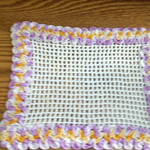 Puede incluir: Cuadrado de crochet blanco con un borde de crochet morado y amarillo.