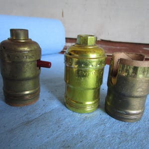 May include: Three brass light bulb sockets, one with a red switch, one with the text "LEVITON" and one with a cardboard insert.