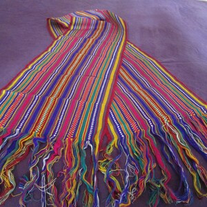 May include: A colorful woven fabric with fringe on the ends. The fabric is made of multiple stripes in shades of red, blue, green, yellow, and white.