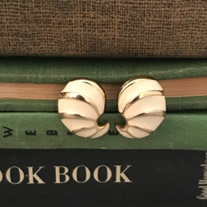 May include: A pair of white and gold tone clip-on earrings. The earrings are shaped like a shell with gold accents.