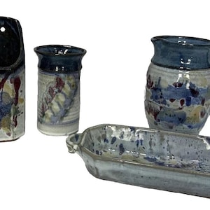 May include: A collection of five ceramic pieces featuring a speckled glaze in shades of blue, white, and brown. The set includes a small vase, a tall wall-mounted planter, a cylindrical cup, a handled pitcher, and an elongated rectangular dish.