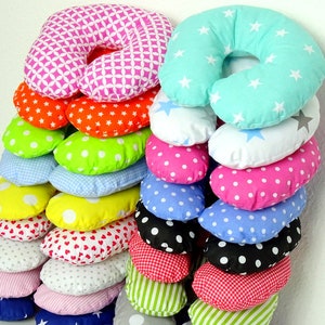May include: A stack of colorful, patterned neck pillows. The pillows feature various designs, including stars, polka dots, hearts, and geometric shapes. Colors include pink, orange, green, blue, yellow, and red. The pillows are designed for comfort and support.