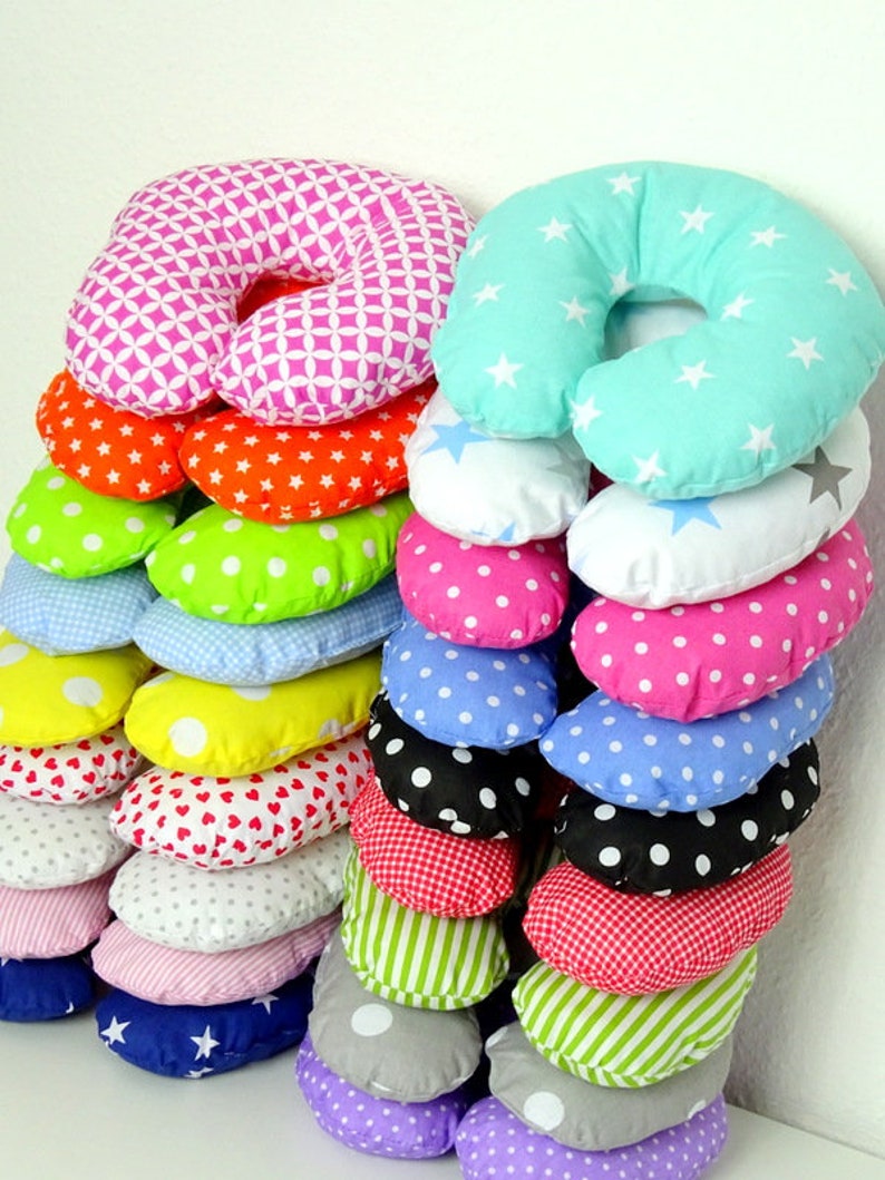 May include: A stack of colorful, patterned neck pillows. The pillows feature various designs, including stars, polka dots, hearts, and geometric shapes. Colors include pink, orange, green, blue, yellow, and red. The pillows are designed for comfort and support.