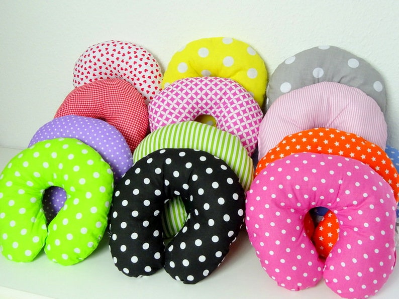May include: A collection of colorful travel neck pillows in various patterns. Pillows include polka dots, hearts, stripes, and geometric designs in shades of pink, green, orange, yellow, and black. The pillows are U-shaped for neck support.