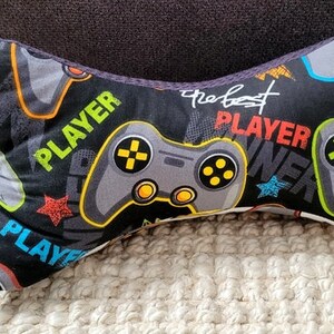 May include: A black and gray gaming pillow with a gray and black gamepad design. The pillow has the text "Player" and "The Best Player" printed on it.