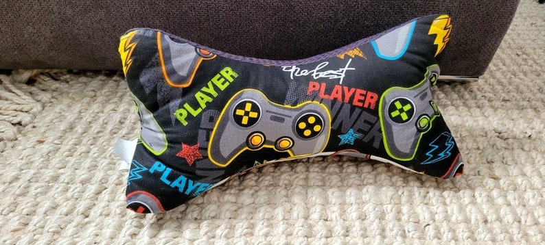 May include: A black and gray gaming pillow with a gray and black gamepad design. The pillow has the text "Player" and "The Best Player" printed on it.