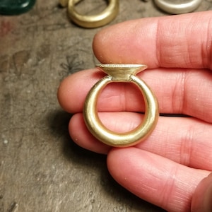 以下が含まれることがあります： 幅広のバンドと丸みを帯びた盛り上がったトップを持つ金のリング。リングは側面から見られており、リングのトップがカメラに向けられています。
