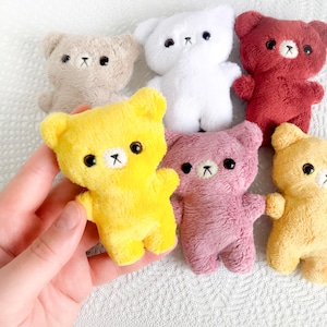 May include: A collection of small, plush teddy bears in various colors, including yellow, pink, white, and red. Each bear has black eyes and a stitched mouth. The bears are soft and fluffy, perfect for a child's toy collection.