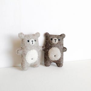 May include: Two handmade felt bear dolls. One is light gray, the other is brown. Both have white bellies, black embroidered eyes and noses, and small arms and ears. The bears are standing upright against a white background.