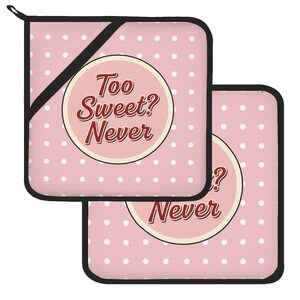 May include: Two square pot holders featuring a light pink background with a white polka dot pattern and black trim. Each pot holder displays a central circular emblem with a cream border containing the dark red text Too Sweet? Never.