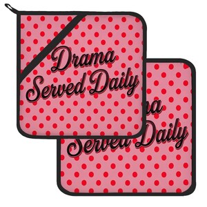 May include: Two square pot holders featuring a pink background with a red polka dot pattern and black trim. The text "Drama Served Daily" is printed in a black cursive font across the center of each pot holder, including a small hanging loop.