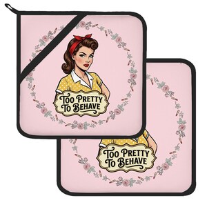 May include: Two square pot holders with a light pink background, featuring a retro-style illustration of a person with a red hair ribbon and yellow polka dot top. A floral wreath with lipstick tubes surrounds the text Too Pretty To Behave.