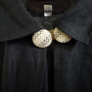 May include: A black linen jacket with two white woven buttons on the collar.
