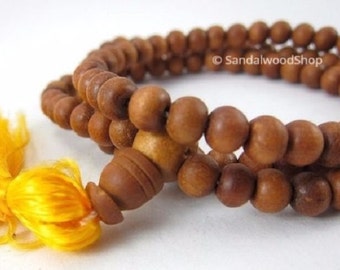May include: A brown sandalwood mala prayer beads necklace with a yellow tassel. The beads are round and smooth, and the tassel is made of a soft, silky material.