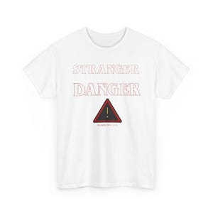 May include: White t-shirt with the words "STRANGER DANGER" in red lettering. Below the text is a red and black road sign with an exclamation point. The text "HEBREWS 11:13" is below the road sign.