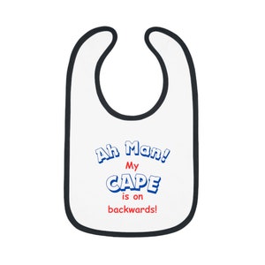 May include: White baby bib with black trim and the text "Ah Man! My CAPE is on backwards!" in blue and red lettering.