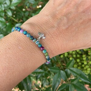 May include: A bracelet made of small, colorful, round beads with a silver bee charm. The bracelet is on a person's wrist.