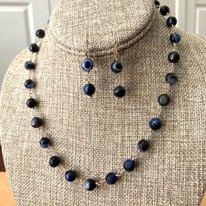 May include: A gold chain necklace and matching earrings with black and blue agate beads. The beads have a swirling pattern and a small blue eye in the center.
